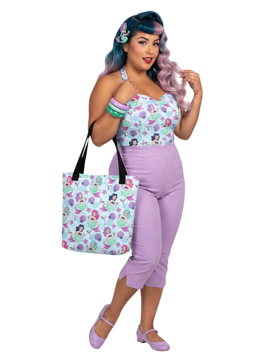 A pinup girl woman wearing a matching mermaid and martini print beach tote bag, lavender purple pinup top and capri pants.