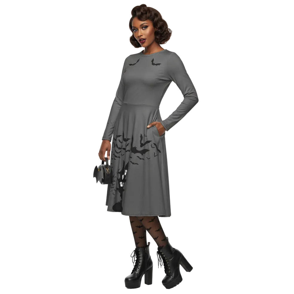 Woman wearing a grey long sleeve goth pinup dress with black bat and haunted house print featuring functional side pockets.
