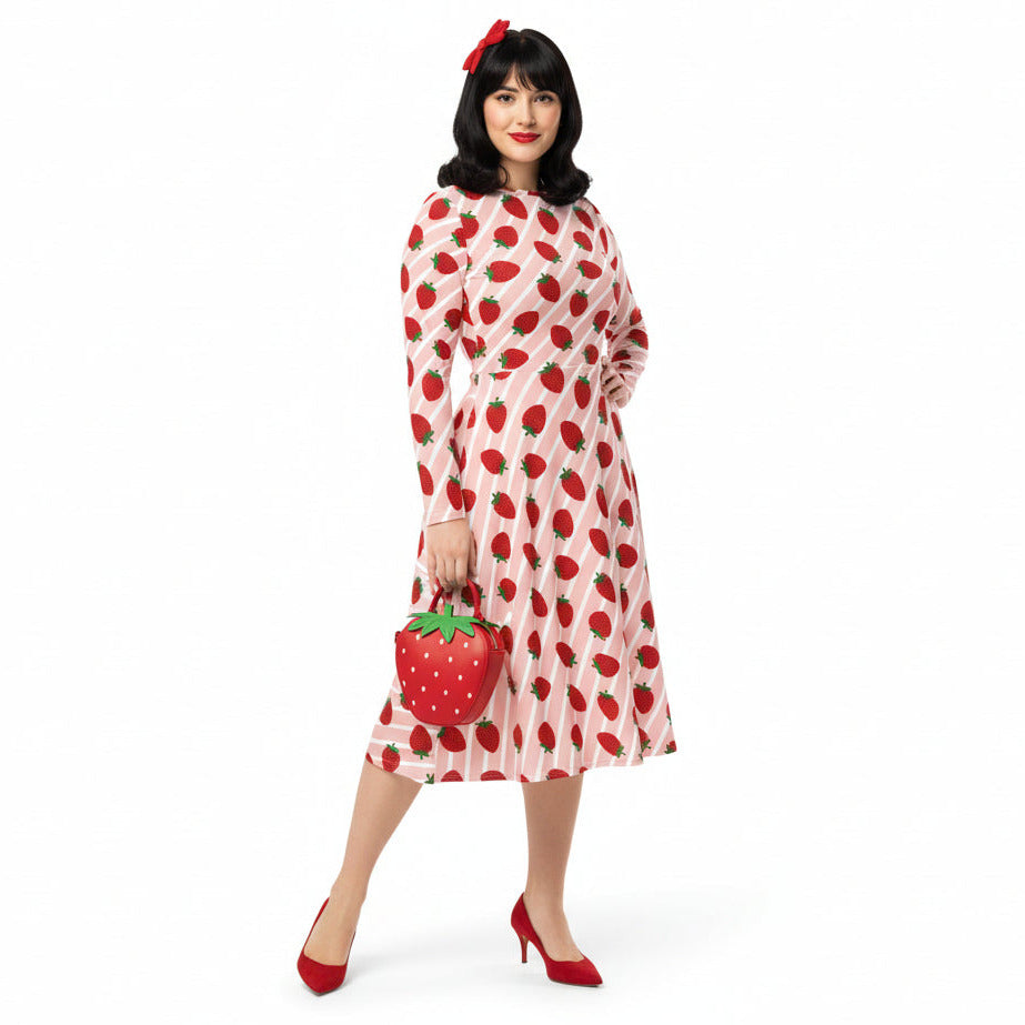 Woman wearing pink and red strawberry print longsleeve dress with pockets on white background