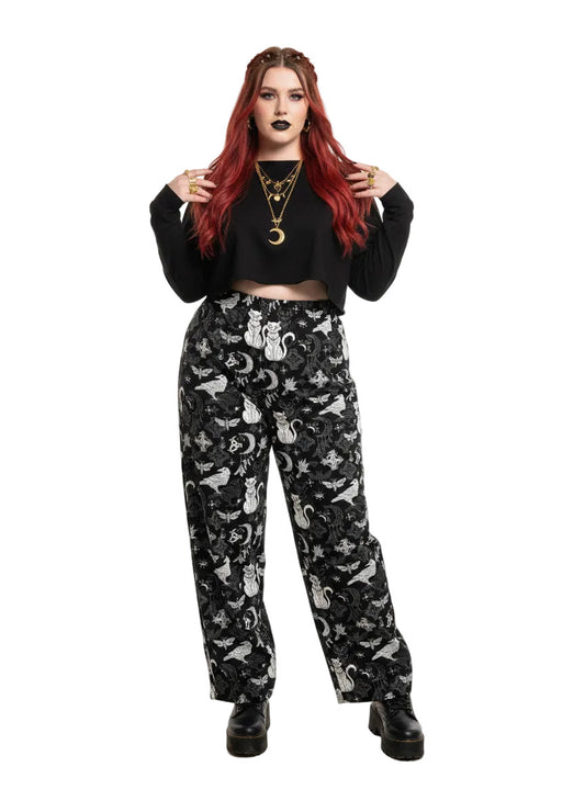 Woman wearing black wide-leg Whimsigoth lounge pants with white celestial cat and moon print.