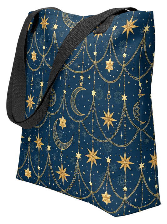 A tote bag with a dark navy blue background and a gold celestial pattern featuring stars, crescent moons, and hanging chains, complete with a black shoulder strap.