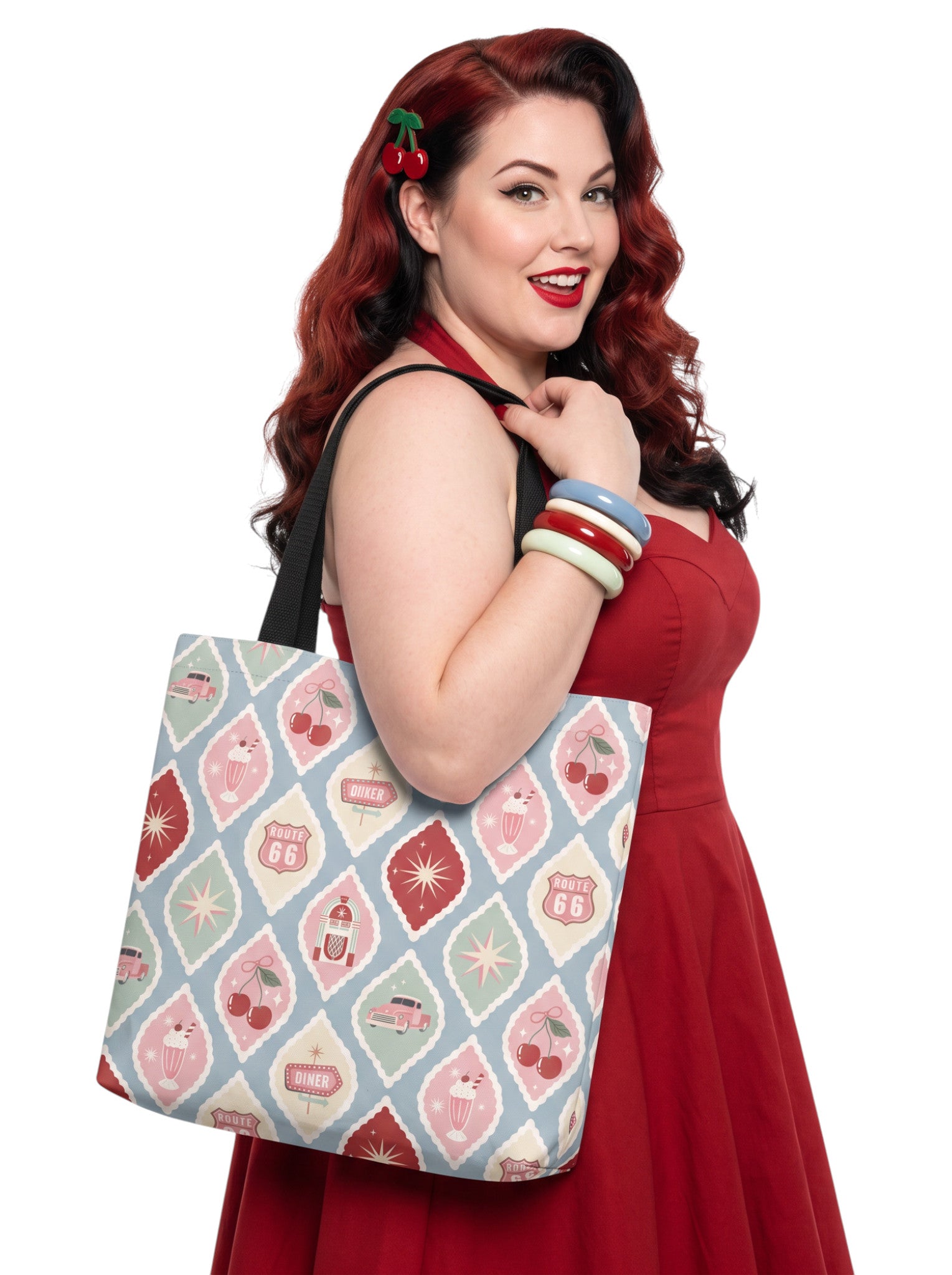 A woman holding a 1950s diner retro tote bag with pastel pinup pattern featuring cherries, milkshakes, and jukeboxes on a light blue background with black straps.