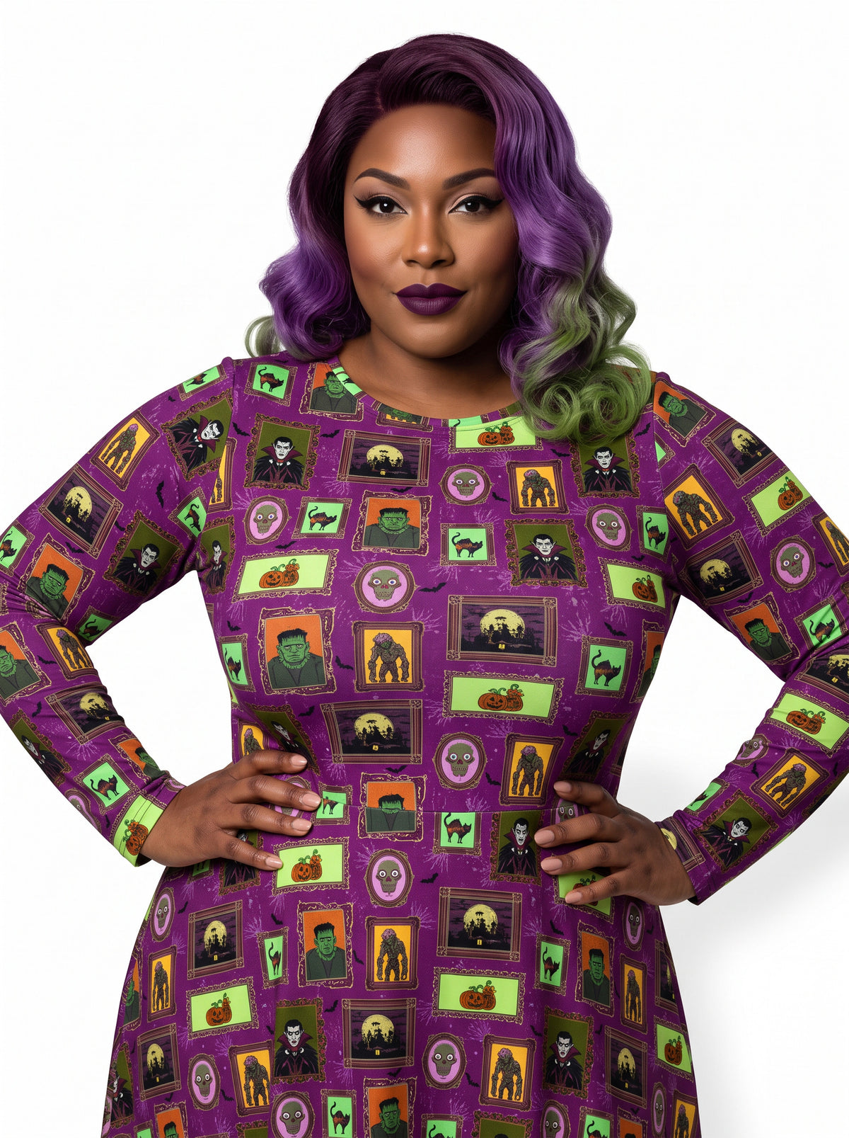 Plus-size model with a purple and lime green ombre Bettie Page hairstyle posing in a 1950s purple gothabilly swing dress featuring spooky monster frames and pumpkins. The long-sleeve, fit-and-flare midi dress is styled with a black corset belt, showcasing a flattering, inclusive curvy fit against a white background.
