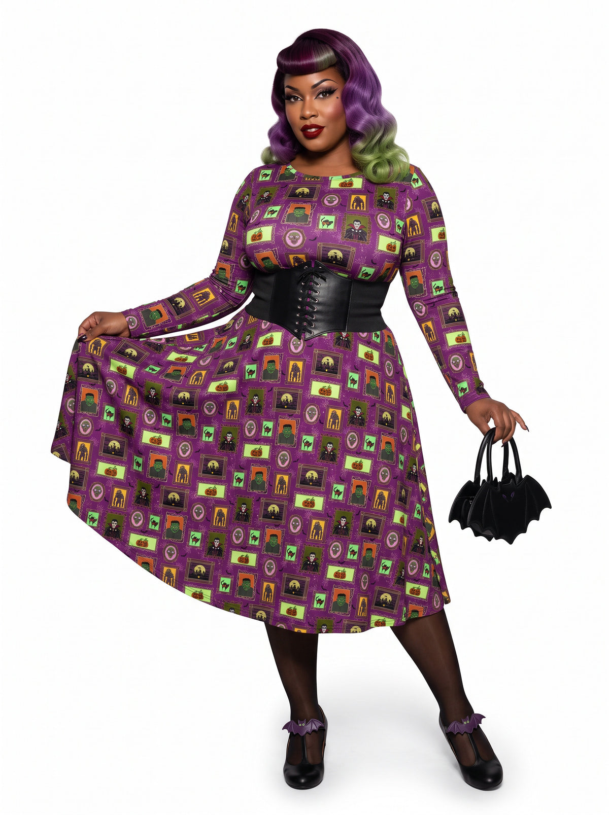 Plus-size model with a purple and lime green ombre Bettie Page hairstyle posing in a 1950s purple gothabilly swing dress featuring spooky monster frames and pumpkins. The long-sleeve, fit-and-flare midi dress is styled with a black corset belt, showcasing a flattering, inclusive curvy fit against a white background.