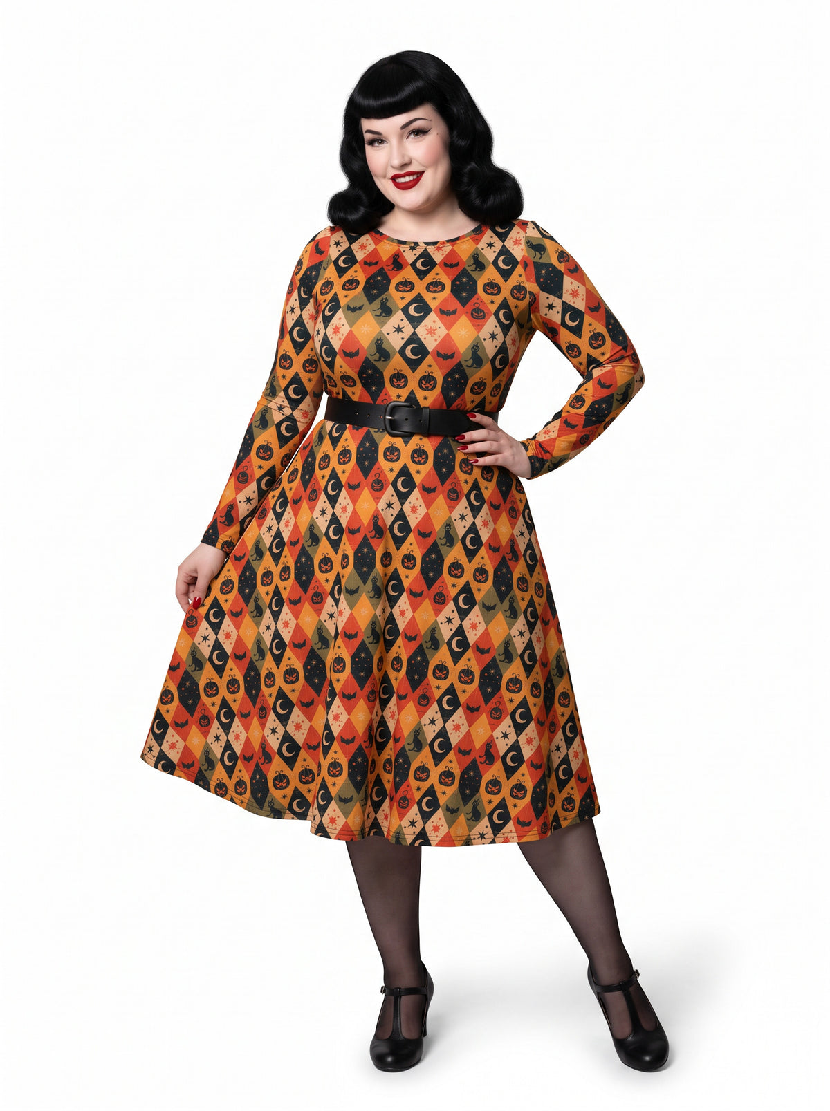 Plus-size model posing in a 1950s-style orange and black harlequin-patterned pinup midi swing dress featuring printed spooky pumpkins, bats, and crescent moons. The vintage-style dress shows a long-sleeve, fit-and-flare silhouette made from a smooth stretch fabric tailored for an inclusive, curvy fit.