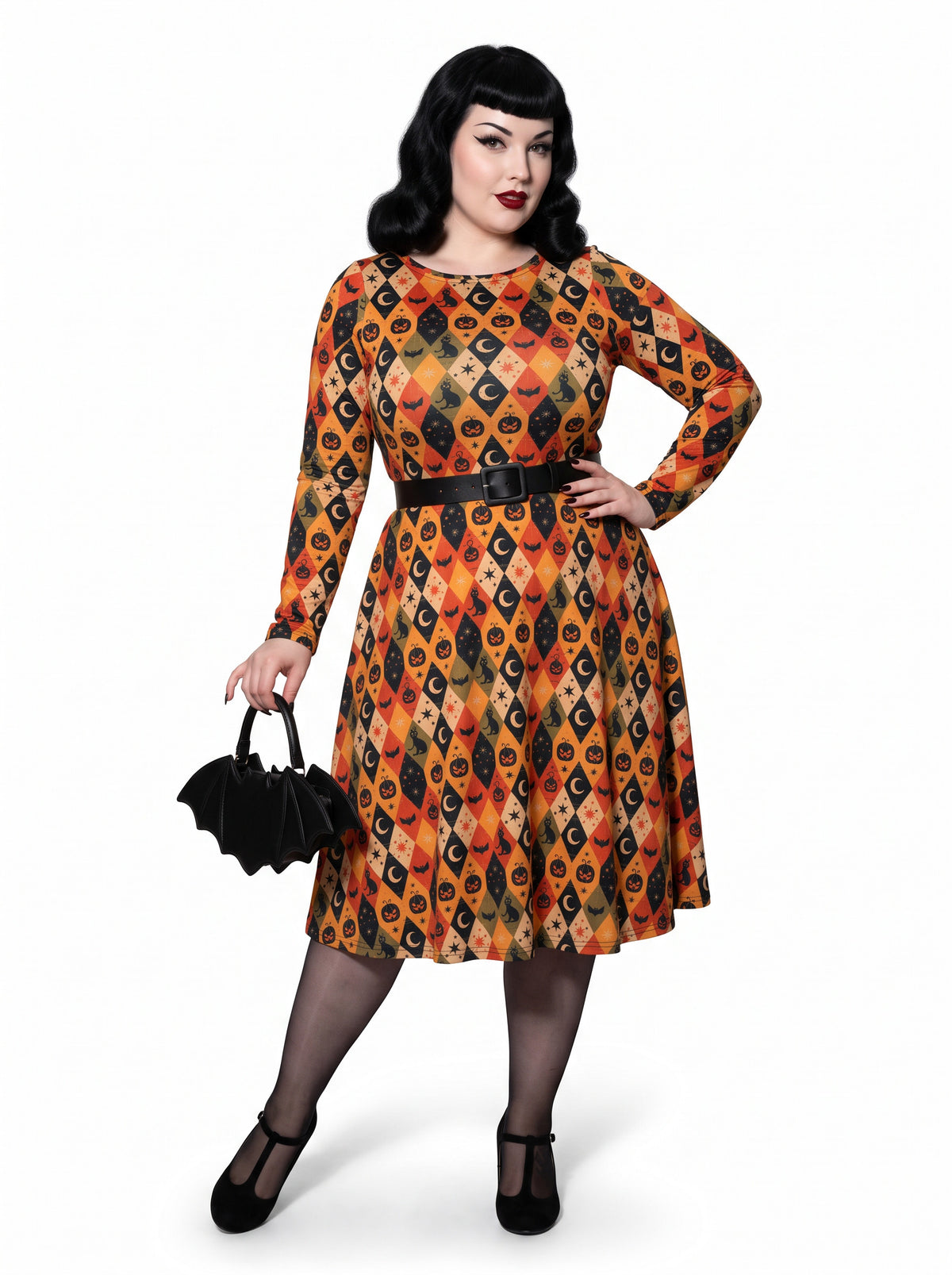 Plus-size model posing in a 1950s-style orange and black harlequin-patterned pinup midi swing dress featuring printed spooky pumpkins, bats, and crescent moons. The vintage-style dress shows a long-sleeve, fit-and-flare silhouette made from a smooth stretch fabric tailored for an inclusive, curvy fit.