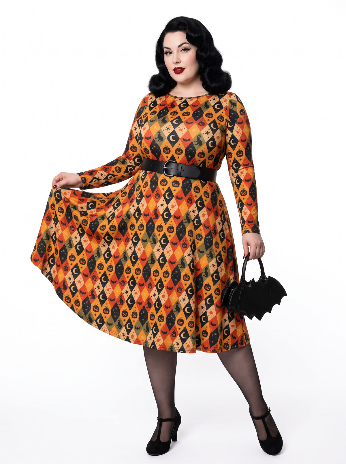 Plus-size model posing in a 1950s-style orange and black harlequin-patterned pinup midi swing dress featuring printed spooky pumpkins, bats, and crescent moons. The vintage-style dress shows a long-sleeve, fit-and-flare silhouette made from a smooth stretch fabric tailored for an inclusive, curvy fit.
