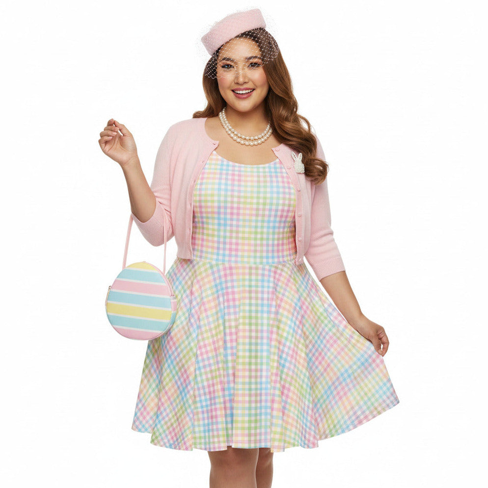 Plus size woman wearing a pastel rainbow gingham 1950s vintage-inspired swing dress with a pink pillbox hat and pearl necklace.