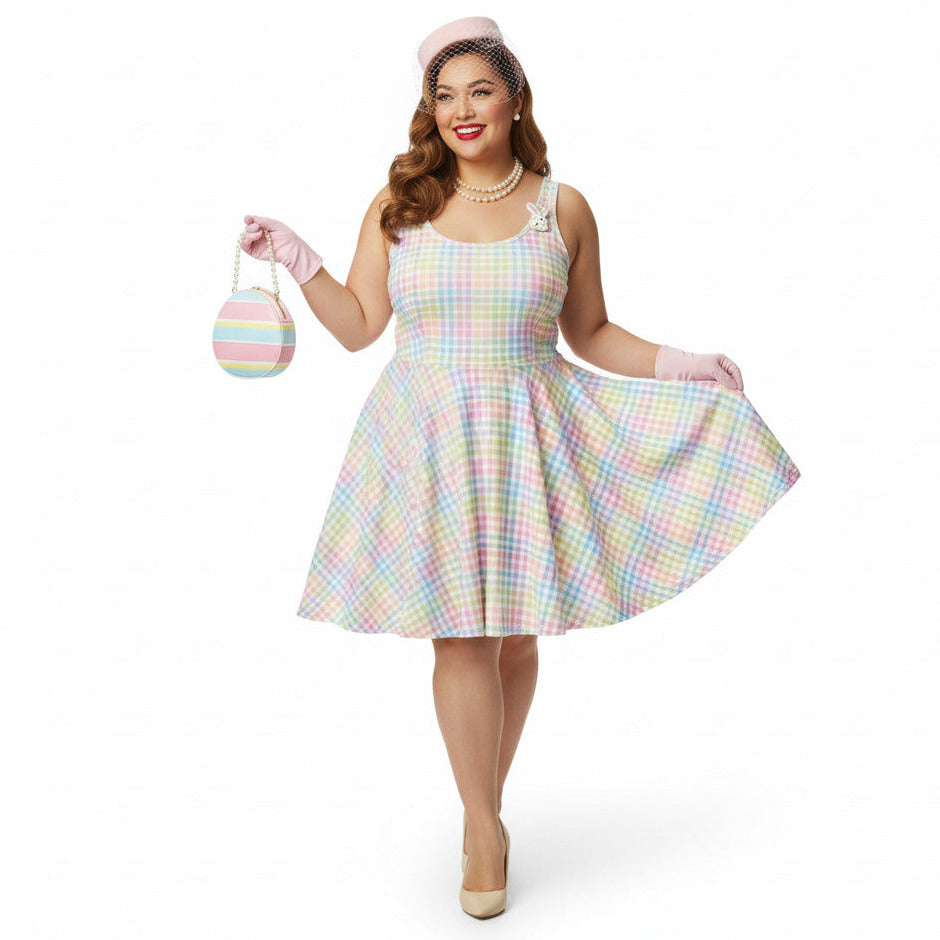Plus size woman wearing a pastel rainbow gingham 1950s vintage-inspired swing dress with a pink pillbox hat and pearl necklace.