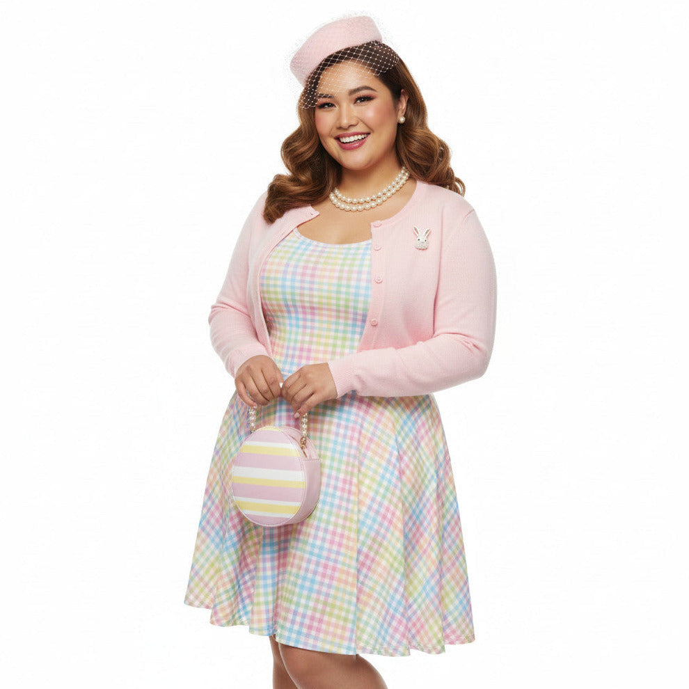 Plus size woman wearing a pastel rainbow gingham 1950s vintage-inspired swing dress with a pink pillbox hat and pearl necklace.