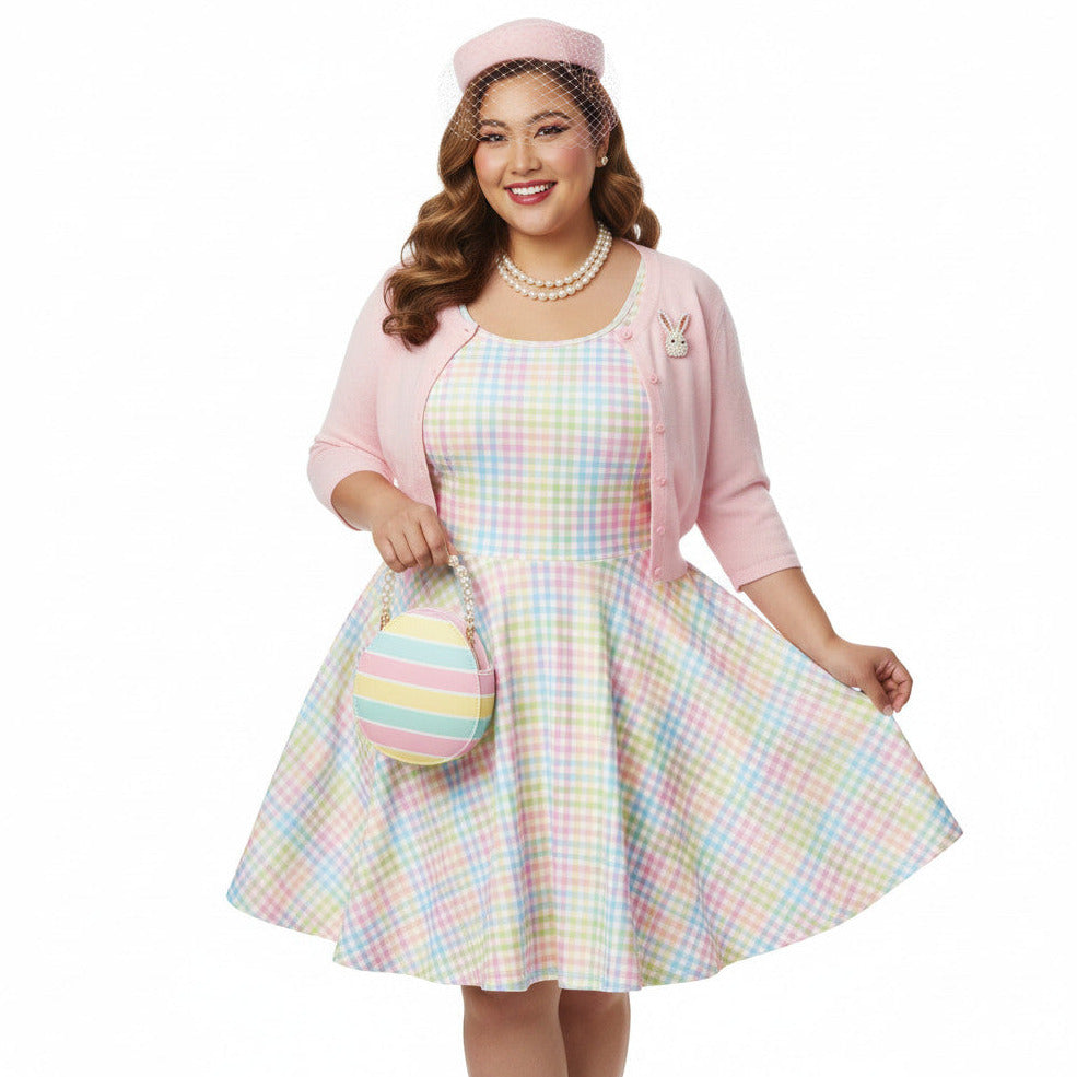 Plus size woman wearing a pastel rainbow gingham 1950s vintage-inspired swing dress with a pink pillbox hat and pearl necklace.