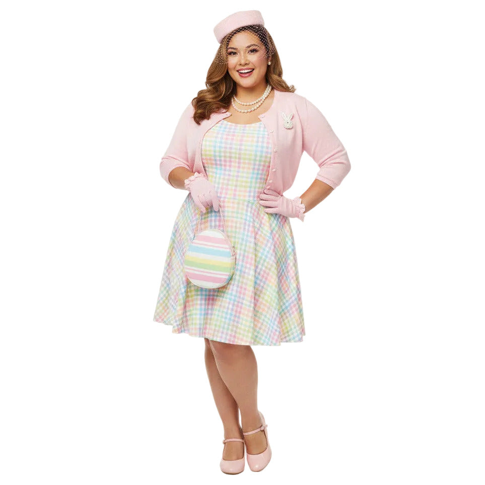 Plus size woman wearing a pastel rainbow gingham 1950s vintage-inspired swing dress with a pink pillbox hat and pearl necklace.