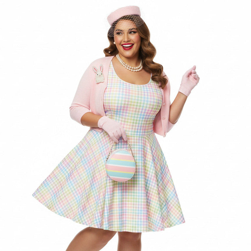 Plus size woman wearing a pastel rainbow gingham 1950s vintage-inspired swing dress with a pink pillbox hat and pearl necklace.