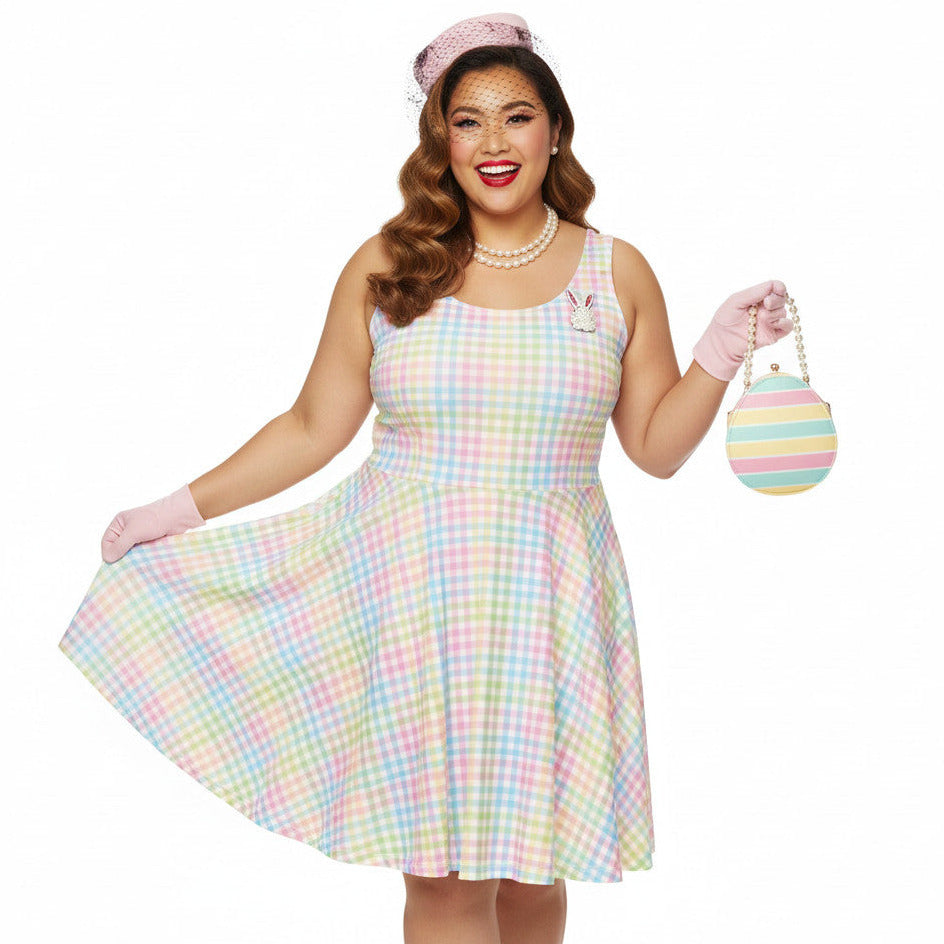 Plus size woman wearing a pastel rainbow gingham 1950s vintage-inspired swing dress with a pink pillbox hat and pearl necklace.