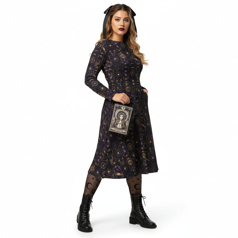 Woman wearing a dark celestial patterned dress with a tarot card clutch on a white background