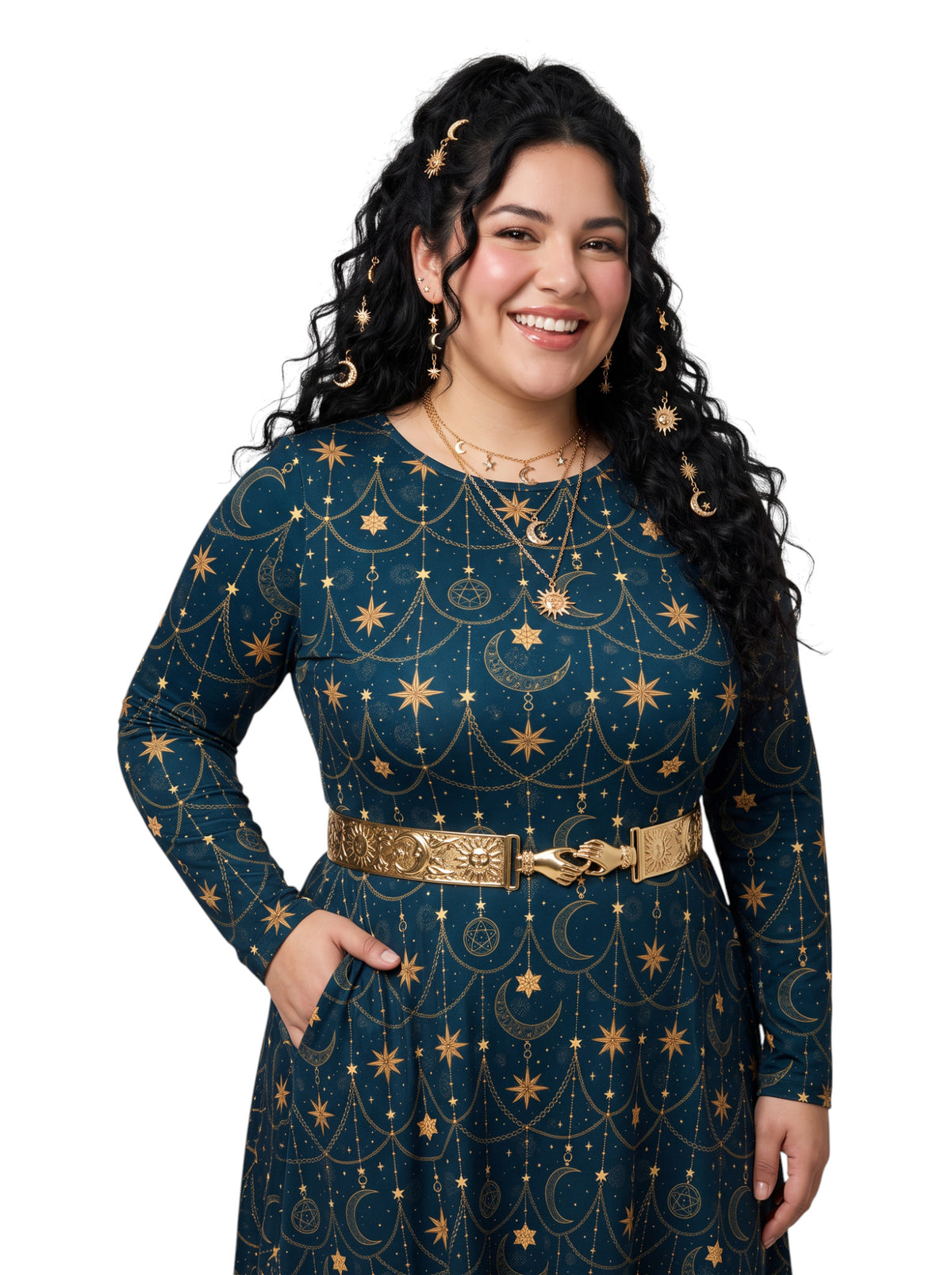 A woman with long, curly black hair wearing a dark teal long-sleeve dress with a gold celestial print of stars, moons, and suns, accessorized with a wide gold belt and gold necklaces, set against a plain white background.