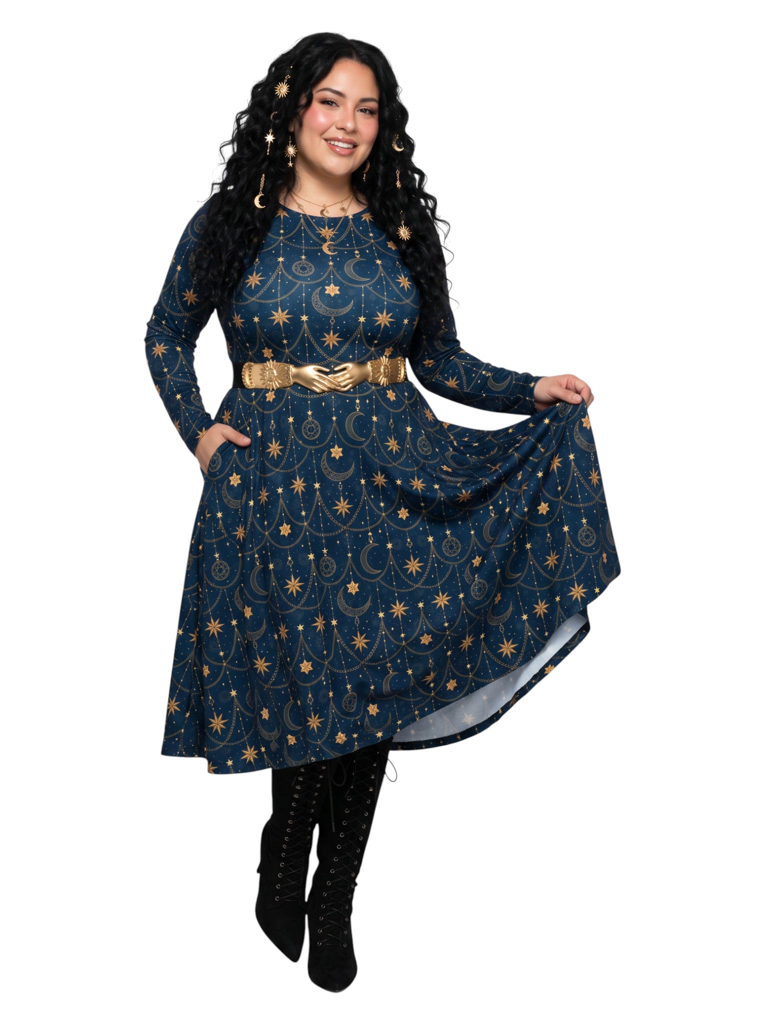 A woman modeling a long-sleeve dark blue dress with a gold celestial print of stars, moons, and suns, accessorized with a wide gold belt, black lace-up boots, and gold statement earrings against a plain white background.
