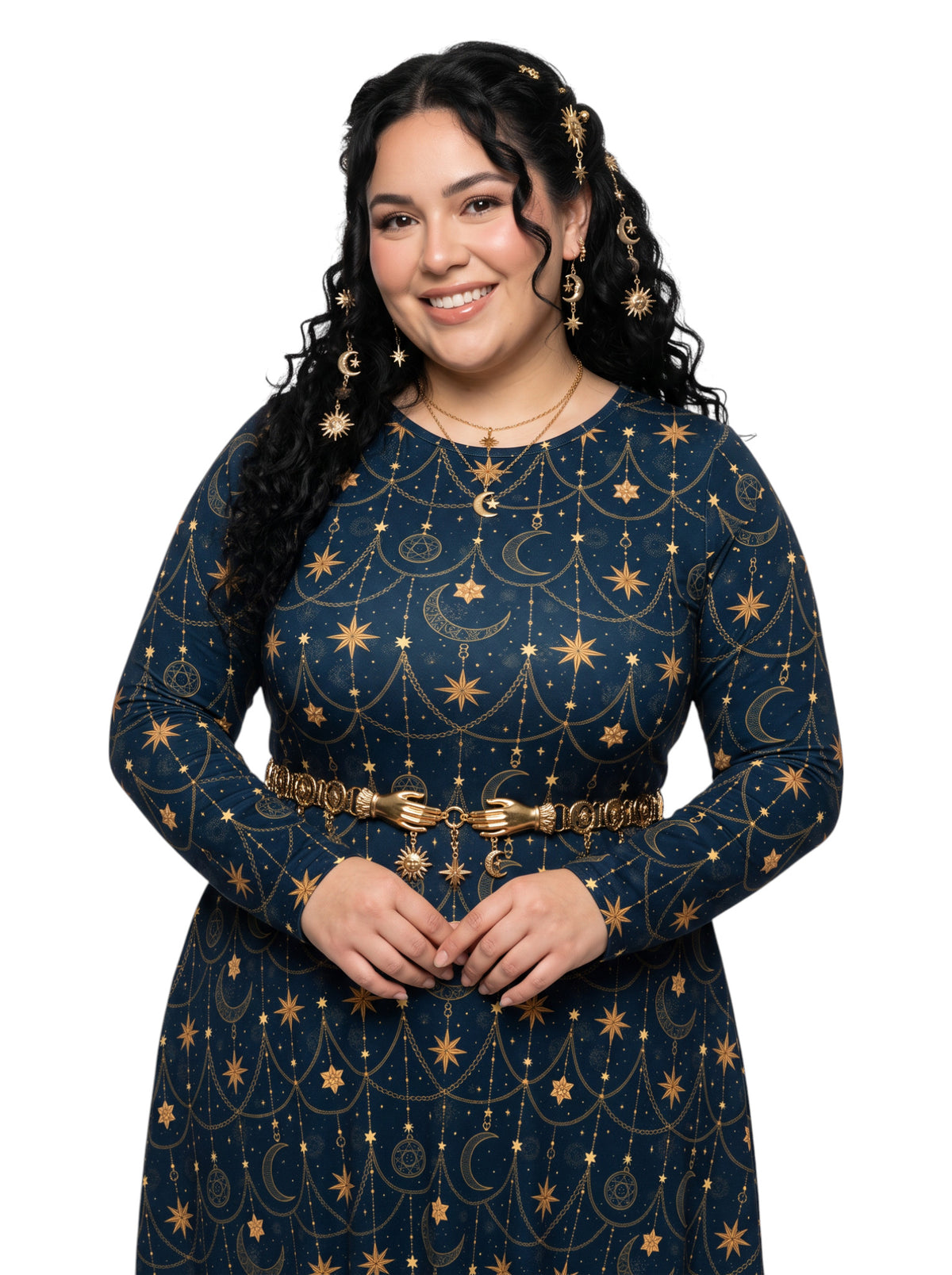 A woman with long, wavy black hair is wearing a long-sleeve navy blue dress decorated with a gold celestial pattern of stars, moons, and constellations. She is accessorized with a gold belt and matching gold earrings, set against a plain white background.