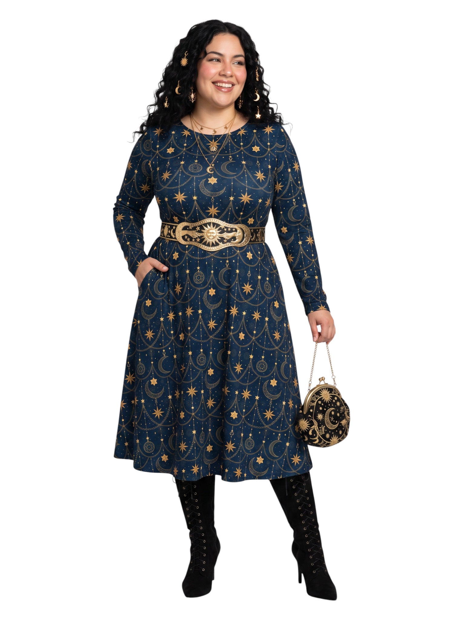 A woman modeling a navy blue long-sleeve midi dress with a gold celestial pattern, a wide gold belt, black lace-up boots, and holding a small gold and black patterned handbag against a plain white background.
