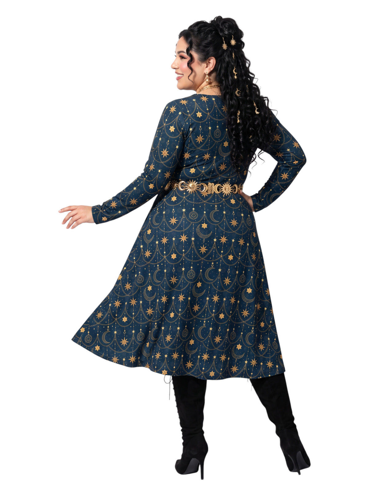 A woman modeling a long-sleeve navy blue tunic dress with a gold celestial pattern of stars and crescent moons, styled with a gold belt and black boots against a white background.