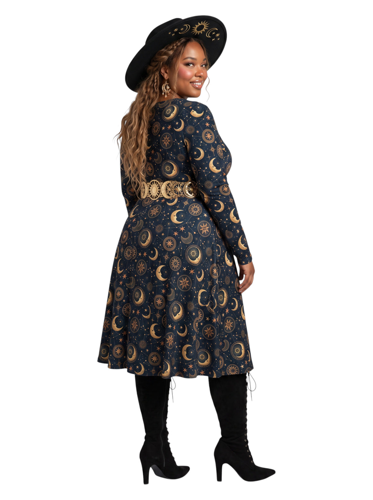 A woman modeling a long-sleeve midi dress with a celestial print of gold crescent moons and suns on a dark navy blue background. She is wearing a wide-brimmed black hat with gold detailing, a matching gold belt, black lace-up knee-high socks, and black high-heeled boots, photographed against a solid white background.
