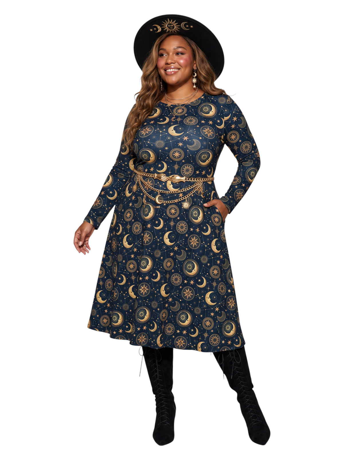 A woman modeling a long-sleeve navy blue dress with a gold celestial print of crescent moons and suns, styled with a gold chain belt, a black wide-brim hat, and black boots against a plain white background.