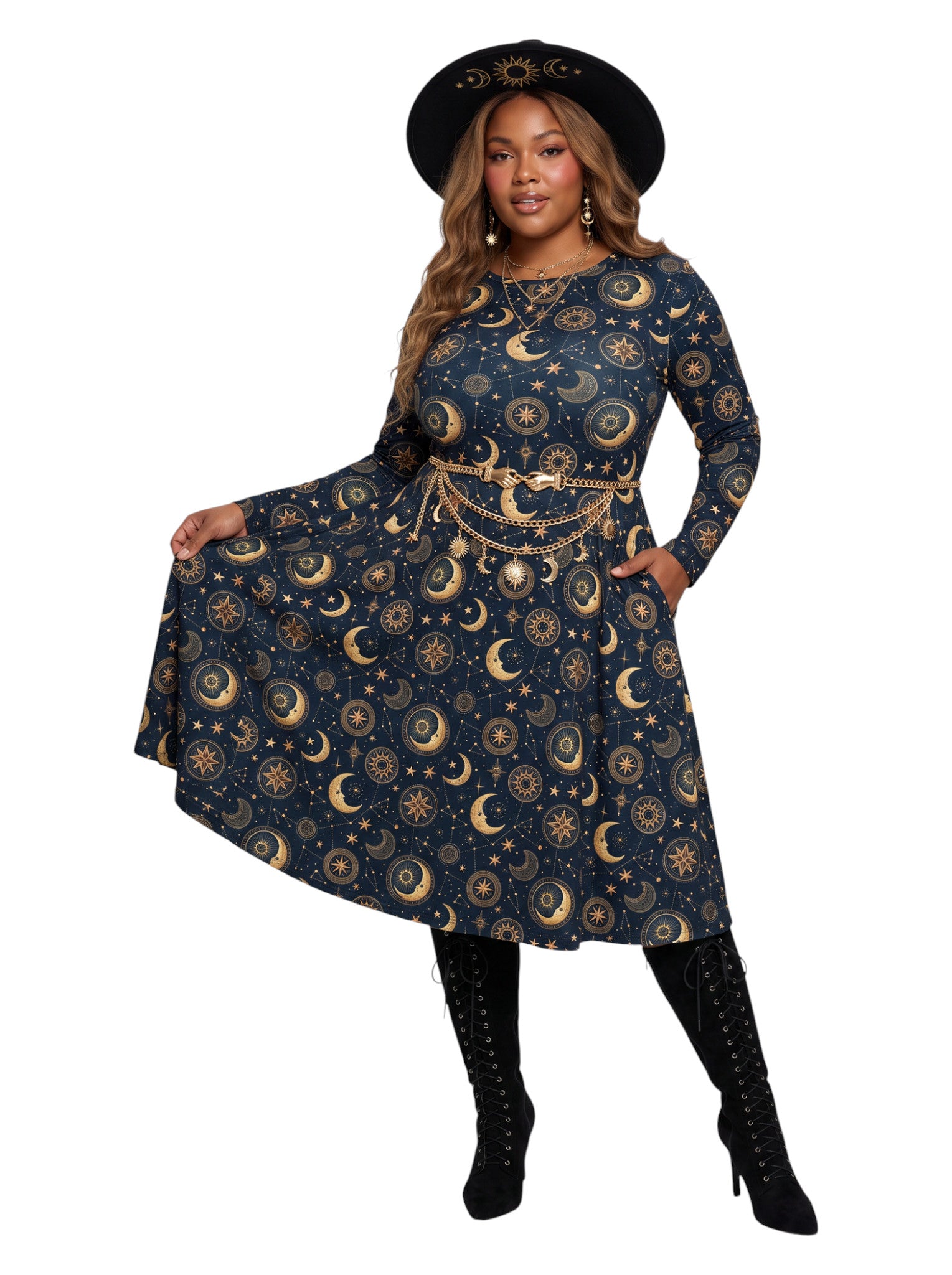 A woman modeling a long-sleeve A-line dress with a celestial print of gold crescent moons and stars on a navy blue background, styled with a gold chain belt, a black hat, and black lace-up boots against a white background.