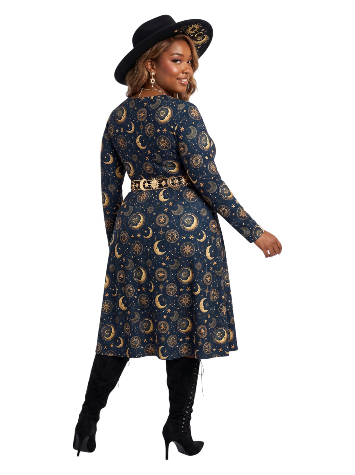 A woman modeling a long-sleeve midi dress with a celestial print of gold crescent moons and stars on a dark navy blue background. She is wearing a matching navy belt with gold buckle details, a black wide-brim hat, and black knee-high boots, photographed against a solid white background.