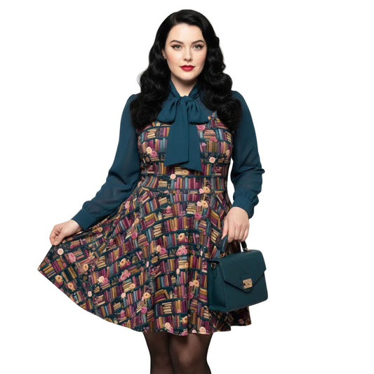 Plus size woman wearing a dark academia bookshelf print skater dress with a green pussy-bow blouse and matching handbag.