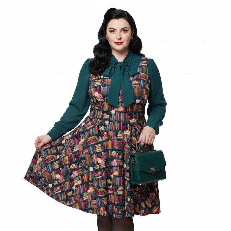Plus size woman wearing a dark academia bookshelf print skater dress with a green pussy-bow blouse and matching handbag.