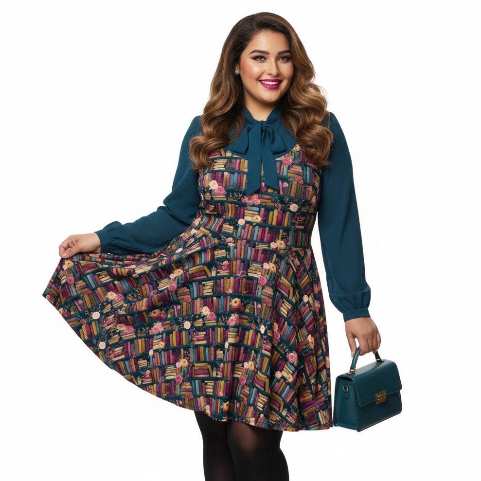 Woman wearing a dark academia bookshelf print skater dress with teal green pussy-bow blouse and matching handbag.