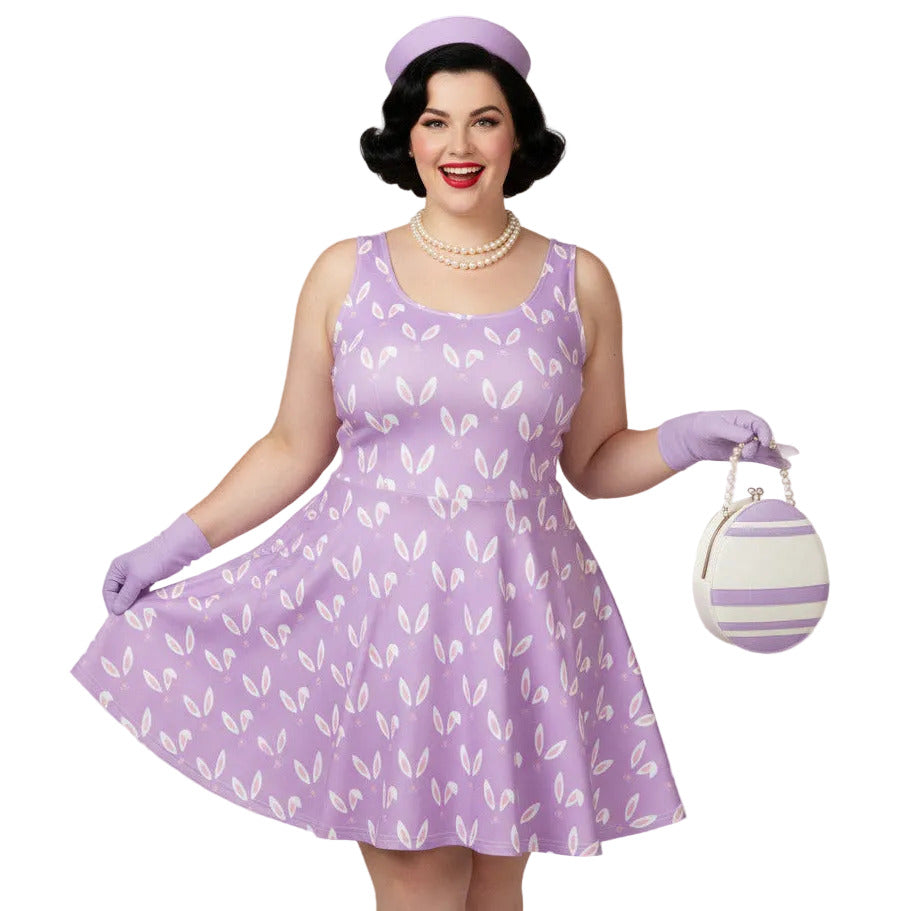 Curvy woman wearing a lavender purple plus size 1950s vintage style swing dress with white Easter bunny print, matching pillbox hat, and pearl necklace.
