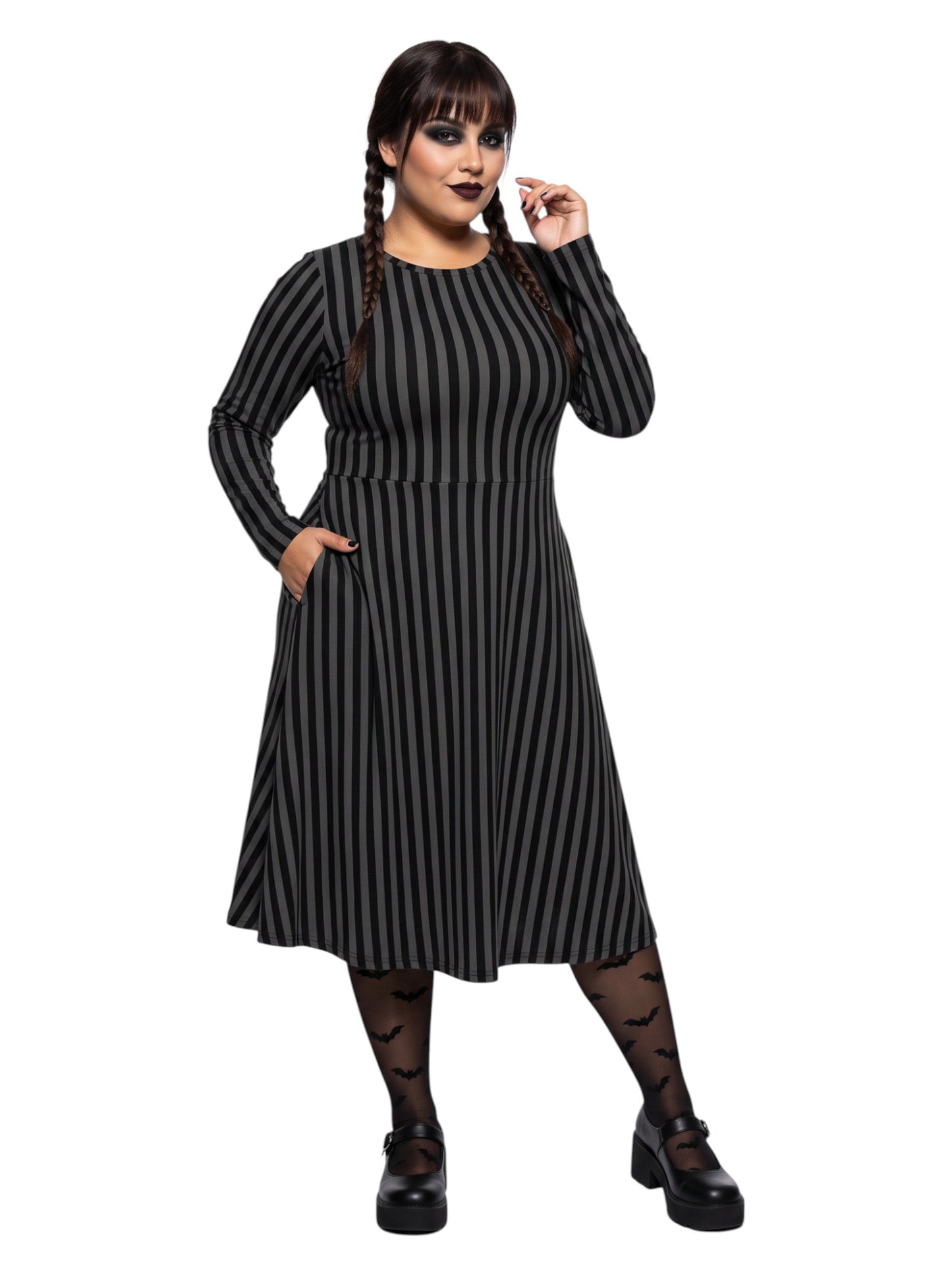 Plus size woman wearing a gothic grey and black vertically striped fit and flare midi dress with long sleeves, functional side pockets, and a scoop neckline.