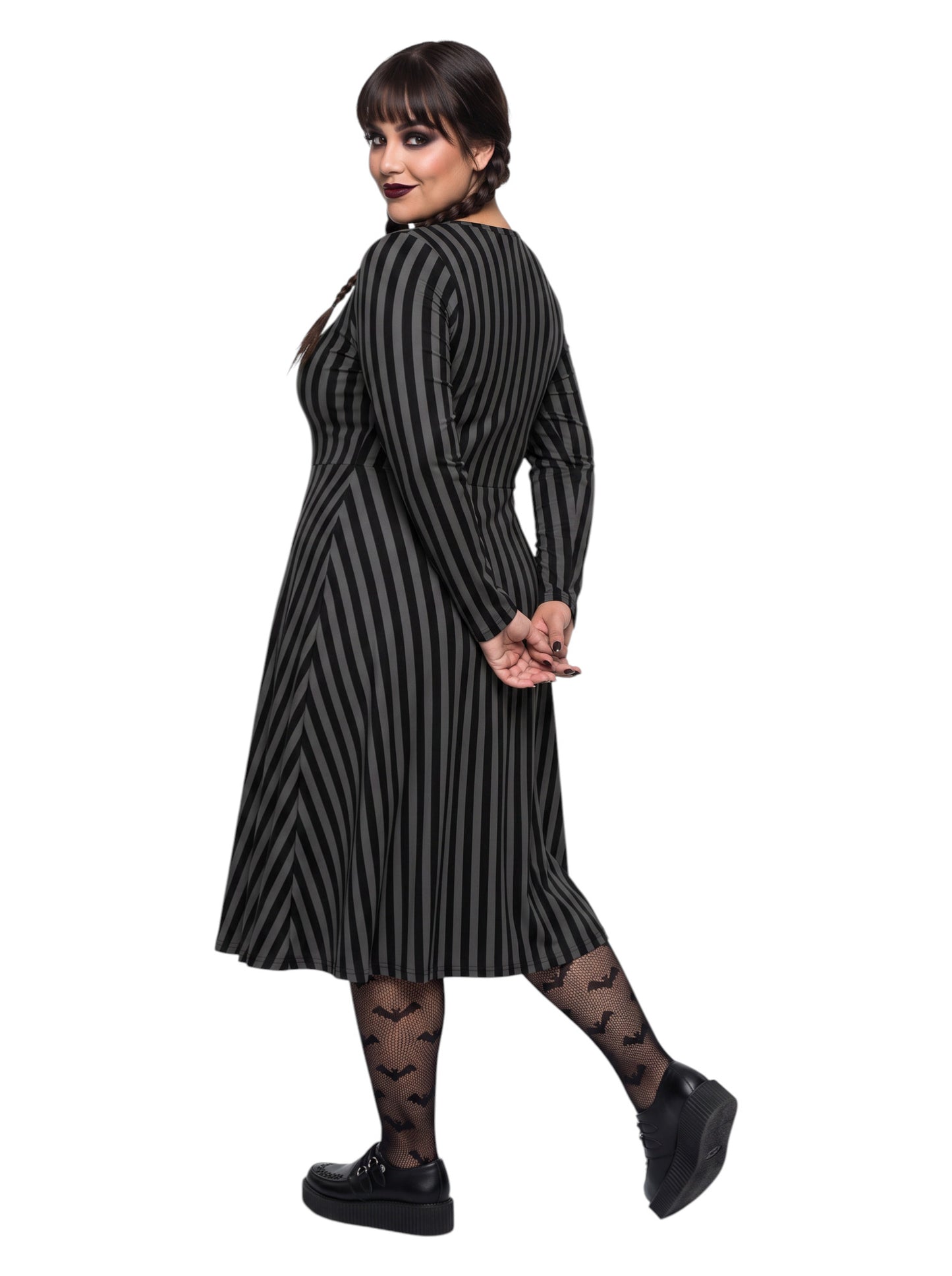Plus size woman wearing a gothic grey and black vertically striped fit and flare midi dress with long sleeves, functional side pockets, and a scoop neckline.