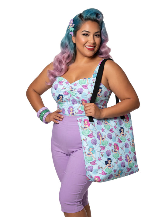 A pinup girl woman wearing a matching mermaid and martini print beach tote bag, lavender purple pinup top and capri pants.
