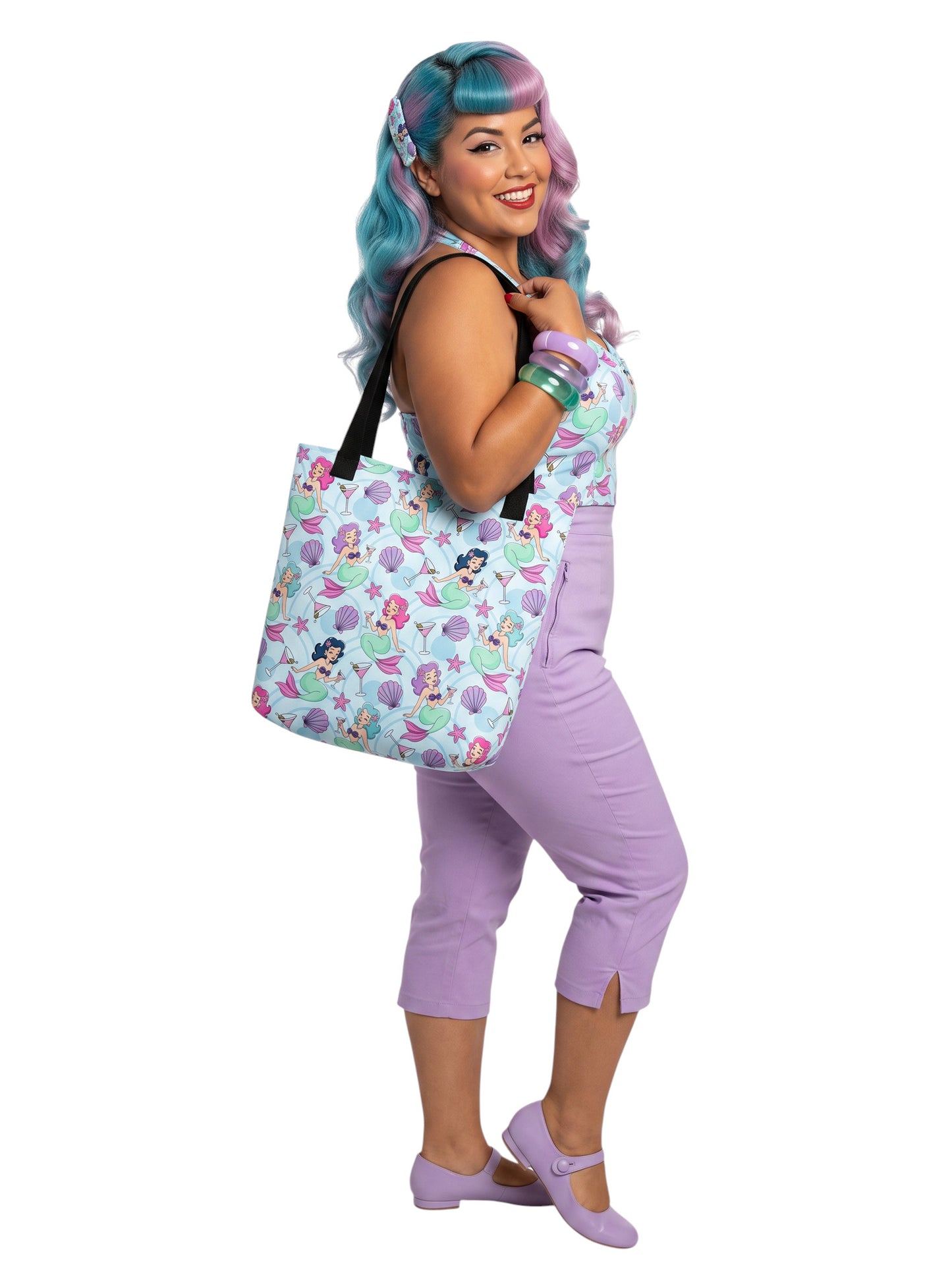 A pinup girl woman wearing a matching mermaid and martini print beach tote bag, lavender purple pinup top and capri pants.