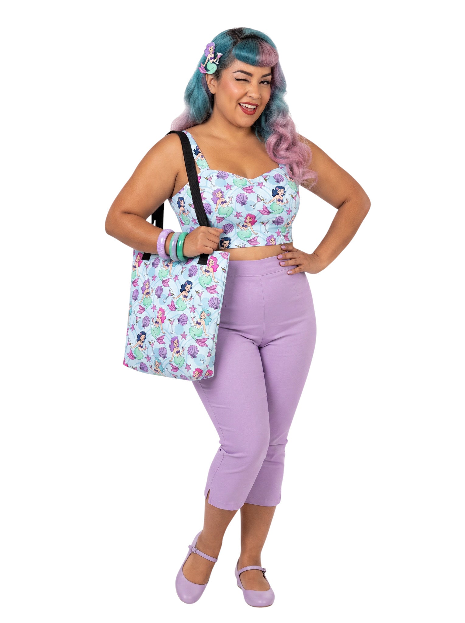 A pinup girl woman wearing a matching mermaid and martini print beach tote bag, lavender purple pinup top and capri pants.