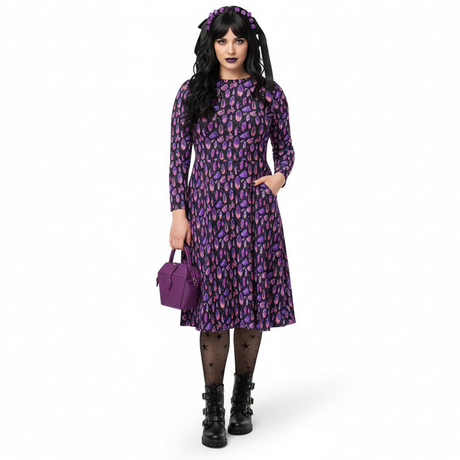Person wearing a purple crystal print  dress with a matching handbag on a white background