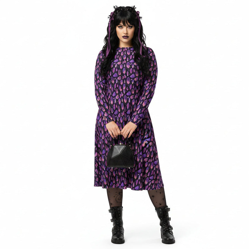 Woman wearing a purple crystal print  dress holding a black handbag on a white background