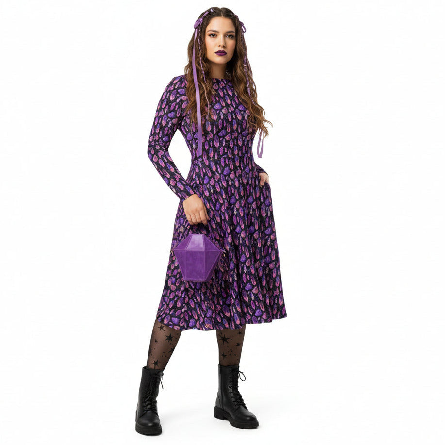 Woman wearing a purple mystical crystal print dress holding a matching handbag on a white background