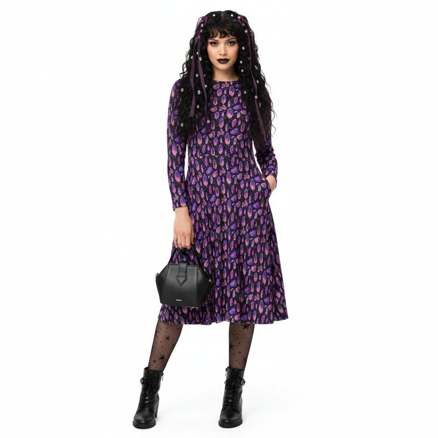 Woman wearing a purple crystal print dress with a black bag on a white background