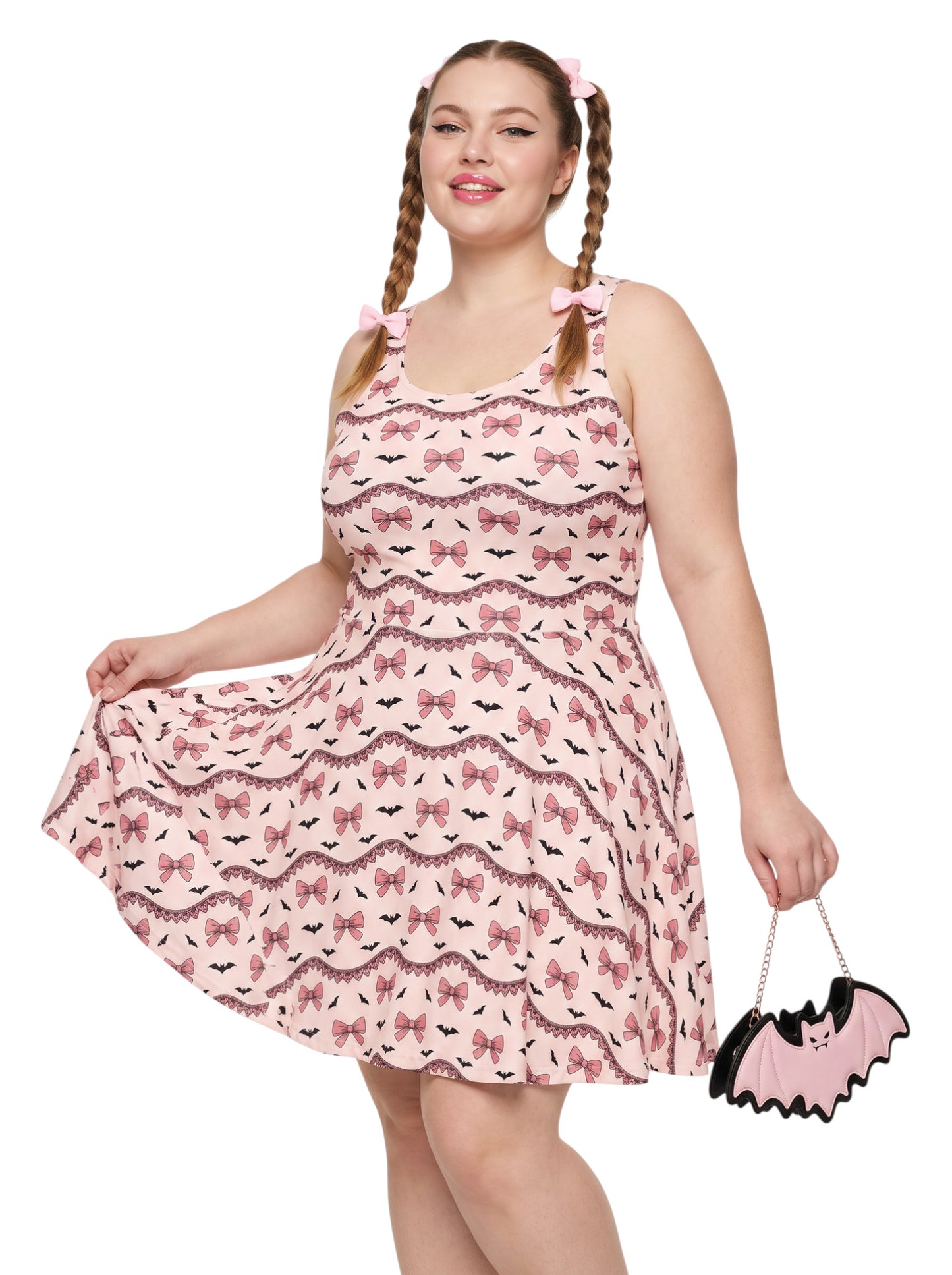 Plus size woman with braided hair wearing a pink sleeveless fit and flare pastel goth coquette dress with a pattern of black spooky bats, pink bows, and lace details.