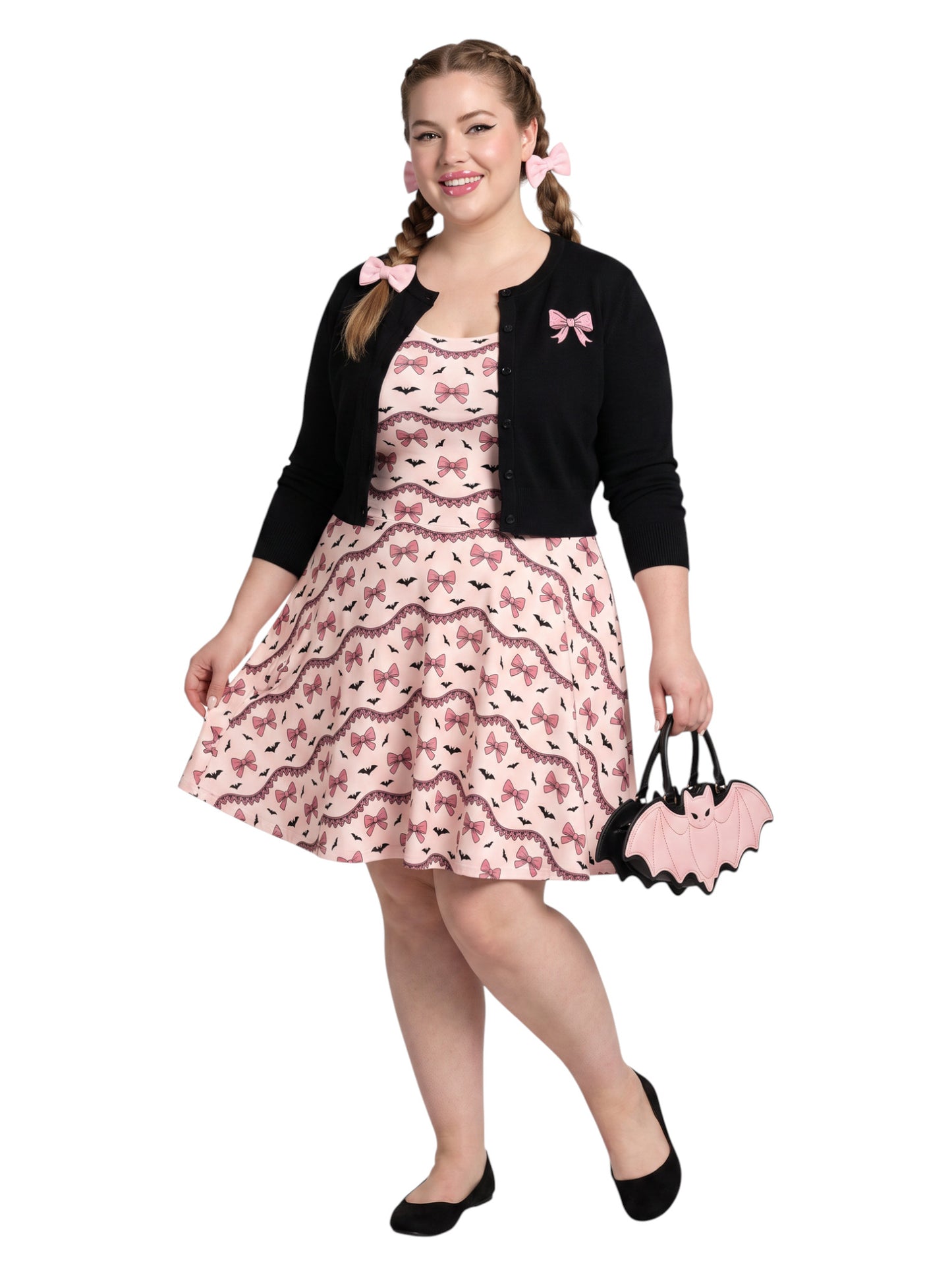 Plus size woman with braided hair wearing a pink sleeveless fit and flare pastel goth coquette dress with a pattern of black spooky bats, pink bows, and lace details.