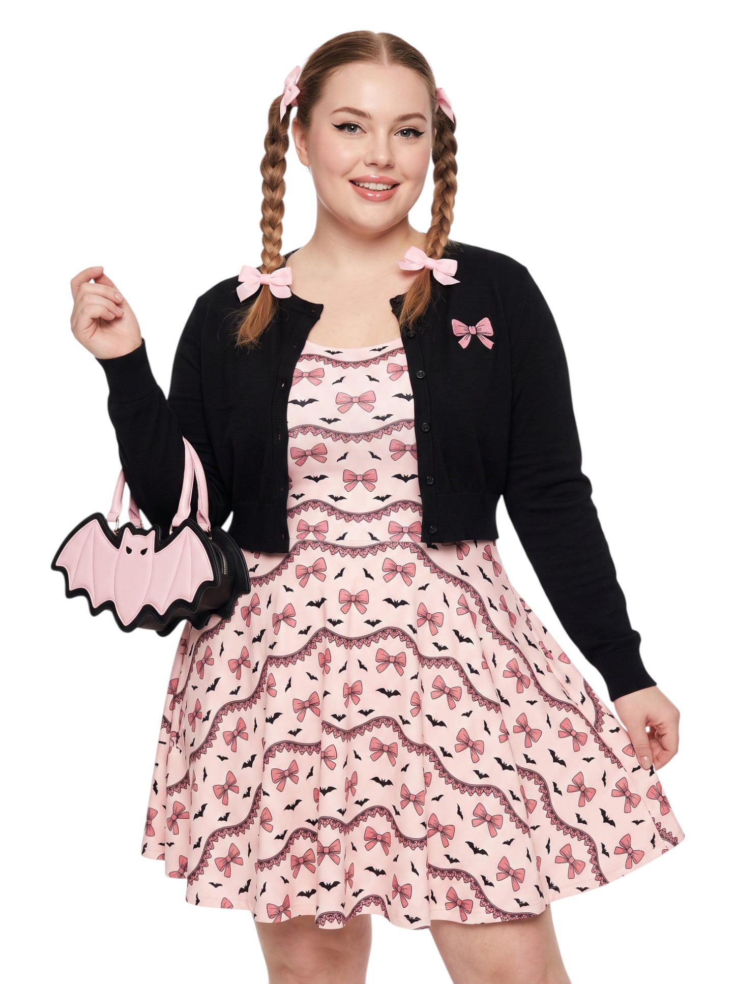 Plus size woman with braided hair wearing a pink sleeveless fit and flare pastel goth coquette dress with a pattern of black spooky bats, pink bows, and lace details.