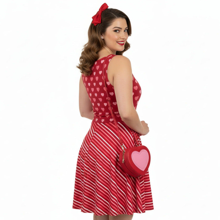 Woman wearing a red dress with heart patterns and holding a matching heart-shaped handbag on a white background