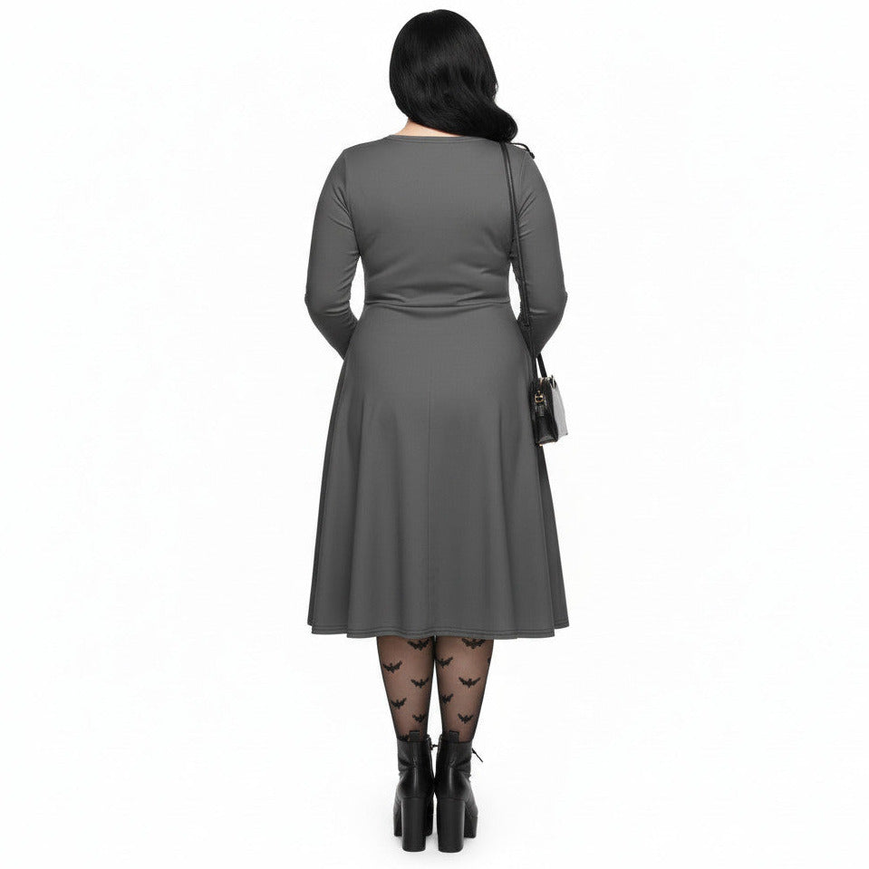 Plus size woman wearing a grey long sleeve goth pinup dress with black bat and haunted house print featuring functional side pockets.