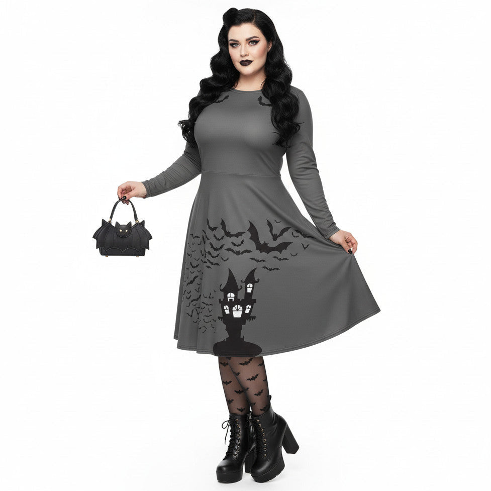 Plus size woman wearing a grey long sleeve goth pinup dress with black bat and haunted house print featuring functional side pockets.