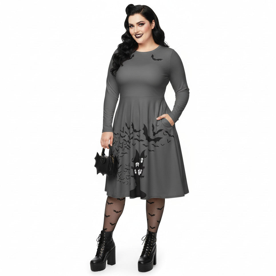 Plus size woman wearing a grey long sleeve goth pinup dress with black bat and haunted house print featuring functional side pockets.