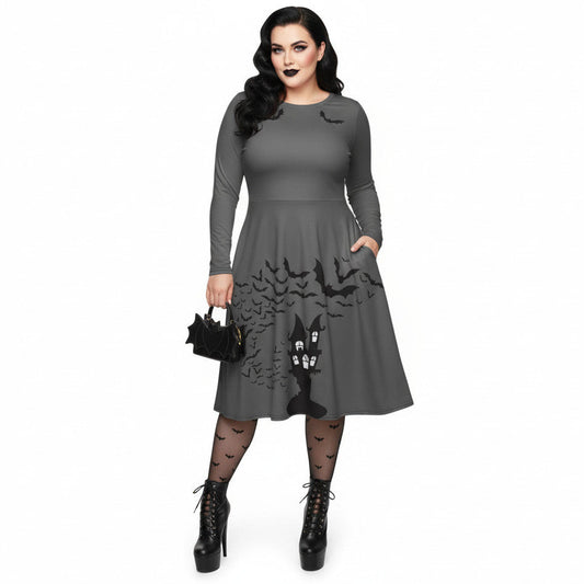 Plus size woman wearing a grey long sleeve goth pinup dress with black bat and haunted house print featuring functional side pockets.