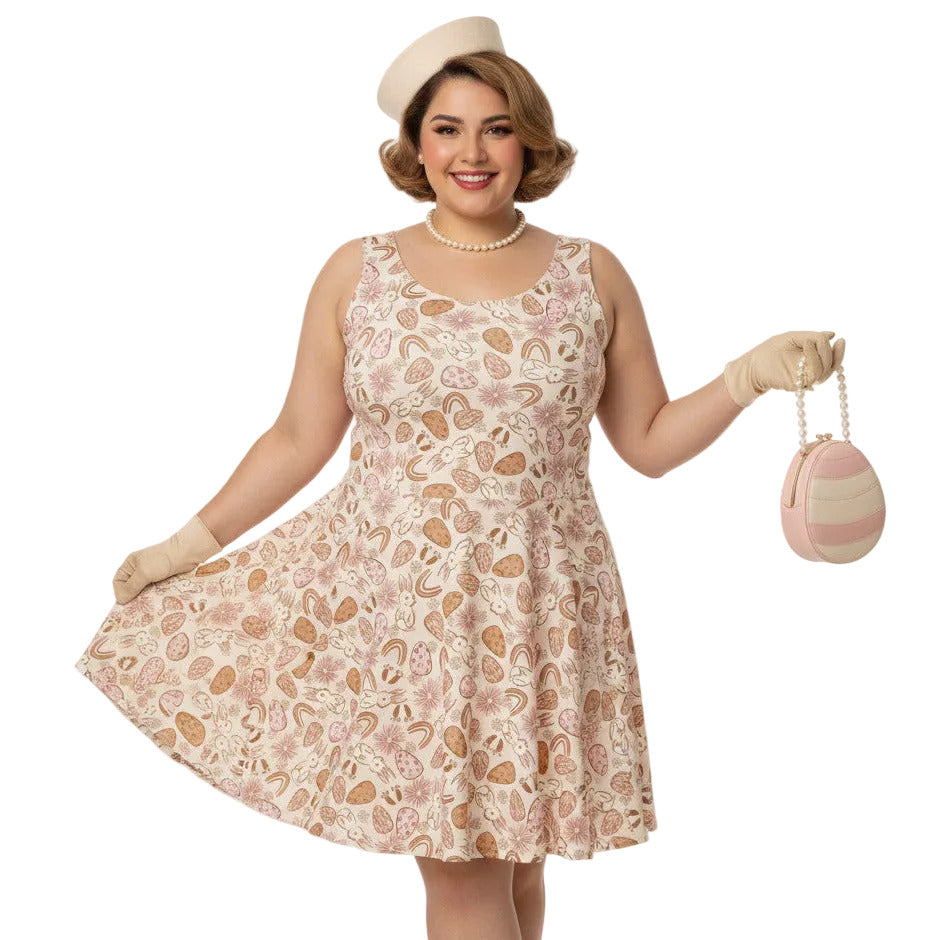 Plus size woman wearing a 1950s vintage style swing dress with pink and tan Easter egg and bunny print, featuring a sleeveless scoop neck and flared skirt.